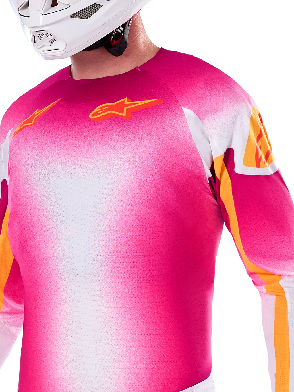 Alpinestars Limited Edition Supertech AFD MIG-tröja, motocross-tröja i en gradient av neonrosa och vitt, med orangea Astars-logotyper och detaljer på ärmarna, bärs av en förare med vit hjälm, atletisk racingpassform.