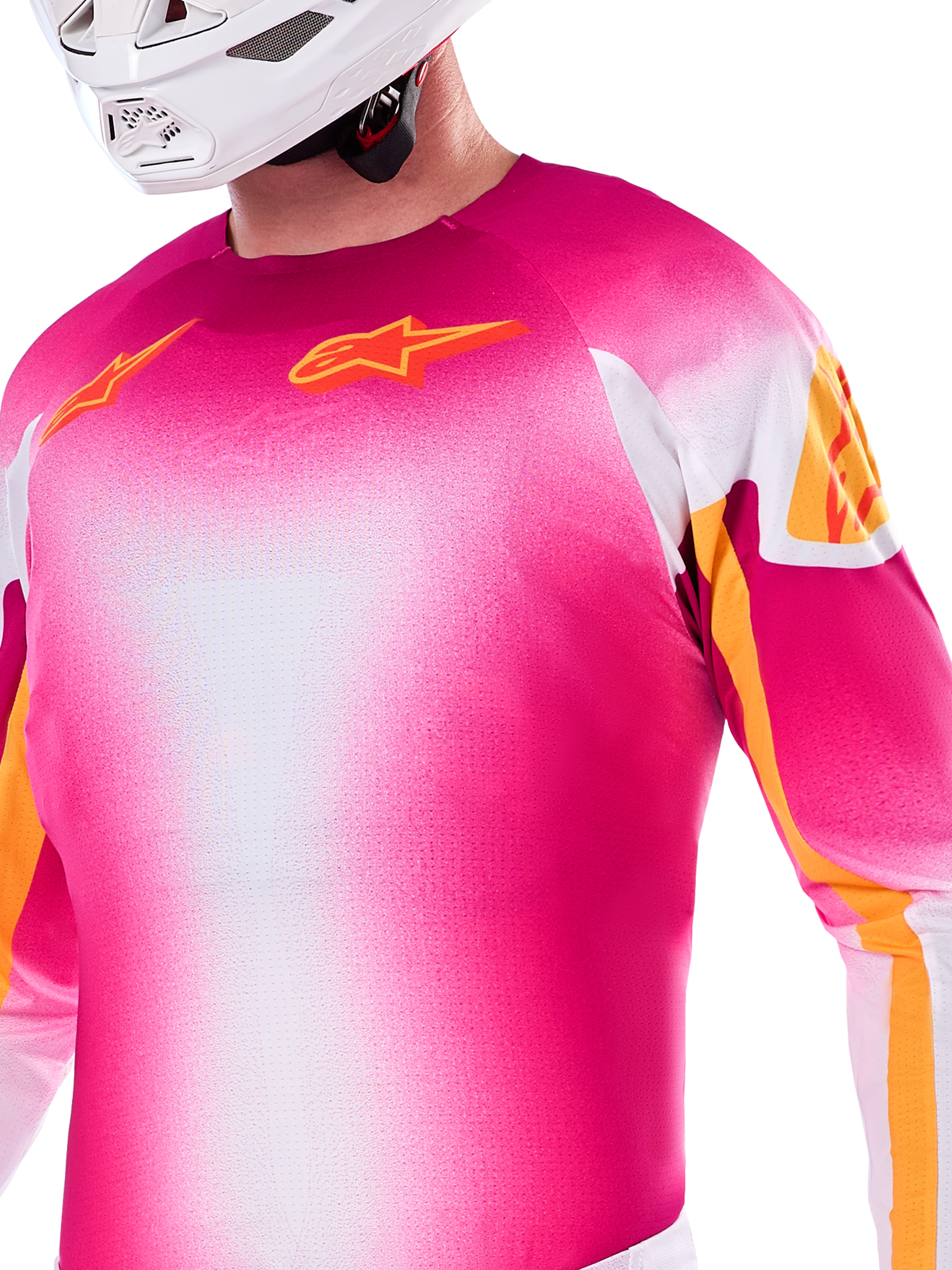 Alpinestars Limited Edition Supertech AFD MIG-tröja, motocross-tröja i en gradient av neonrosa och vitt, med orangea Astars-logotyper och detaljer på ärmarna, bärs av en förare med vit hjälm, atletisk racingpassform.