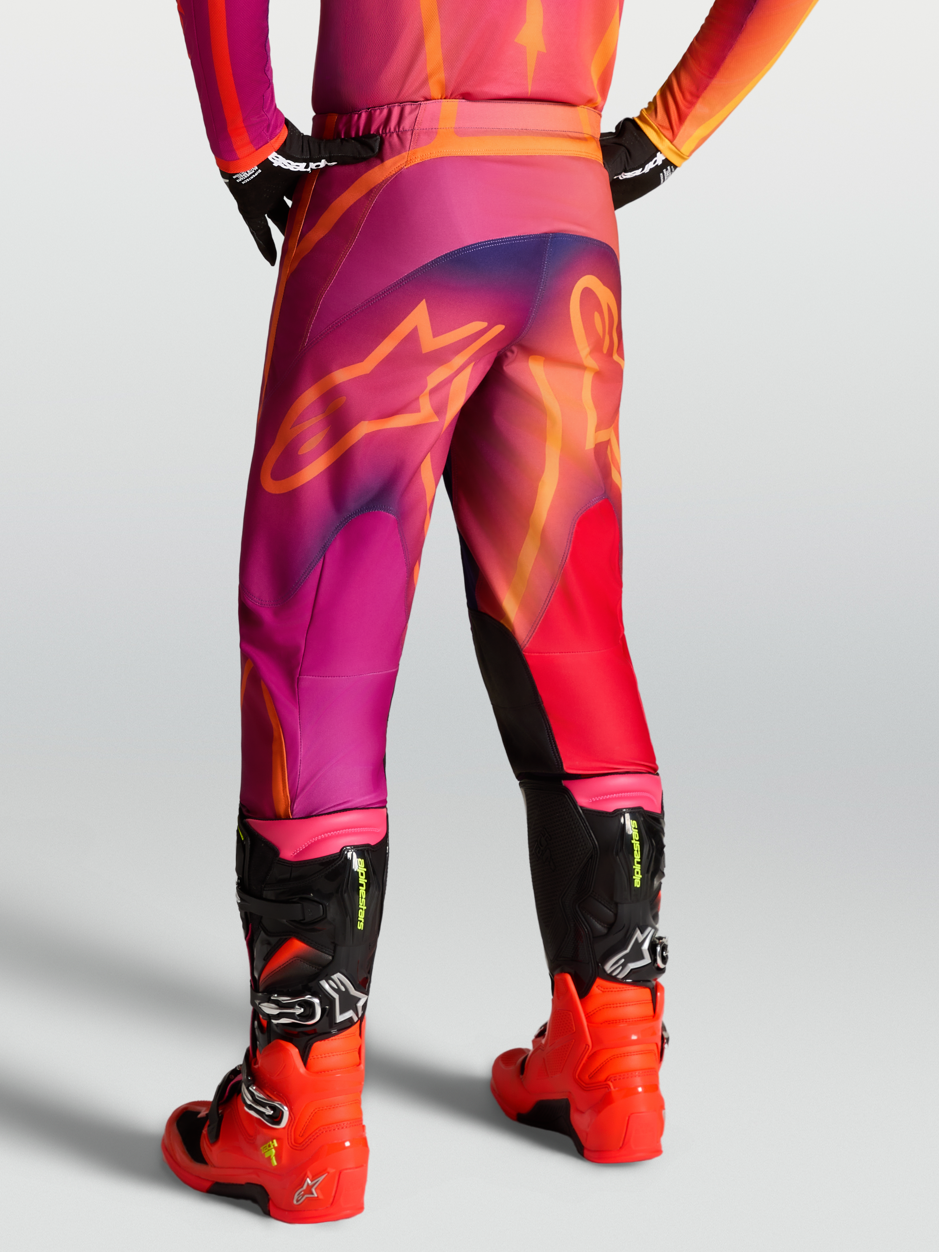 Alpinestars Fluid Kepler byxor, motocrossbyxor för herr, lila och orange, bakifrån på modell med matchande tröja och röda motocrossstövlar, 600D polytyg och förböjd design.