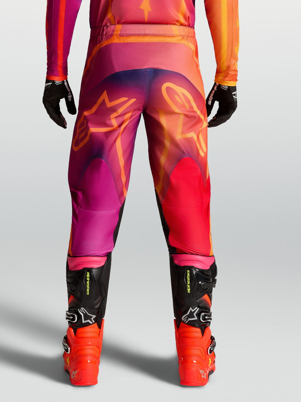 Alpinestars Fluid Kepler byxor, motocrossbyxor för herr i lila och orange med stjärngrafik bak och svarta racingstövlar.