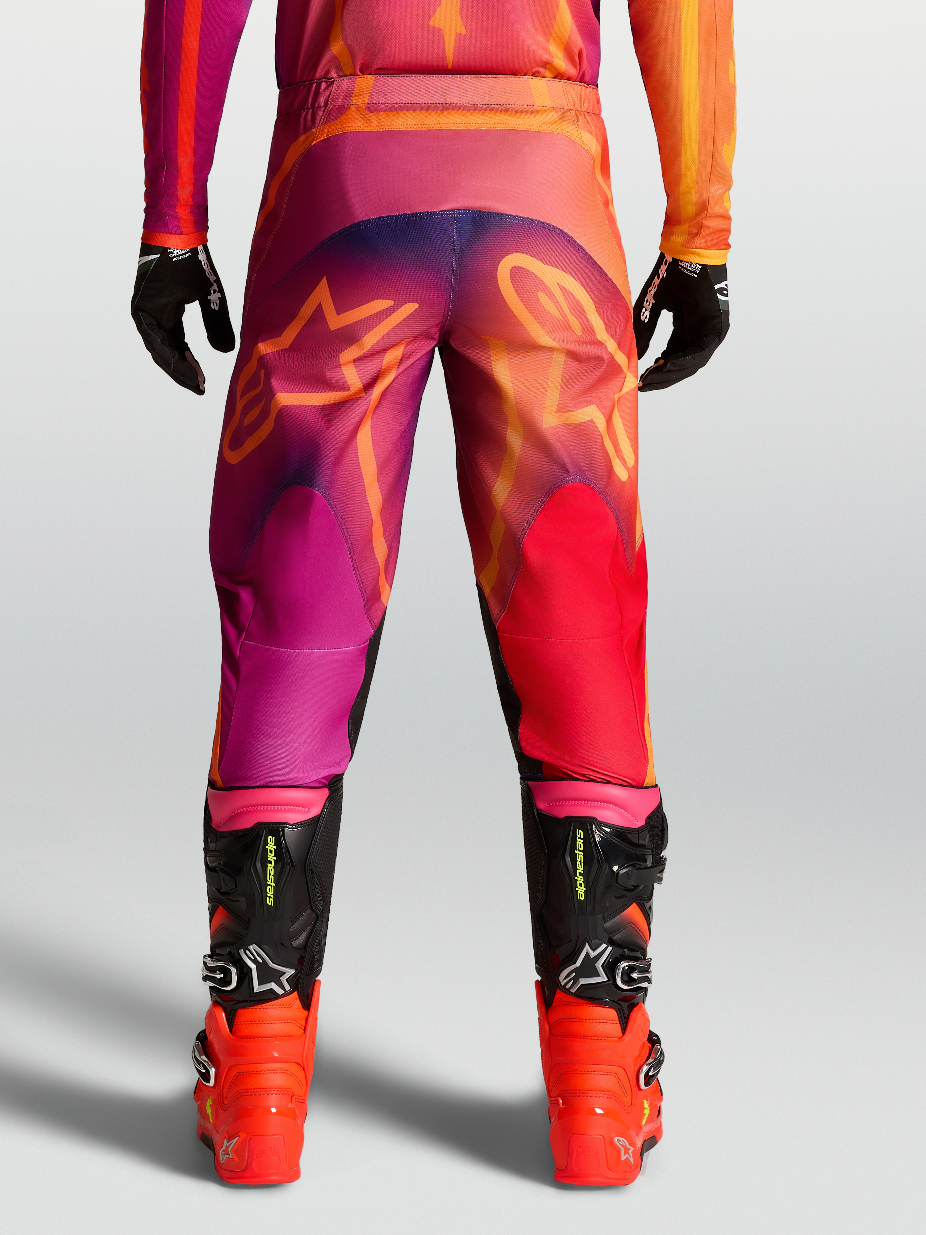 Alpinestars Fluid Kepler byxor, motocrossbyxor för herr i lila och orange med stjärngrafik bak och svarta racingstövlar.