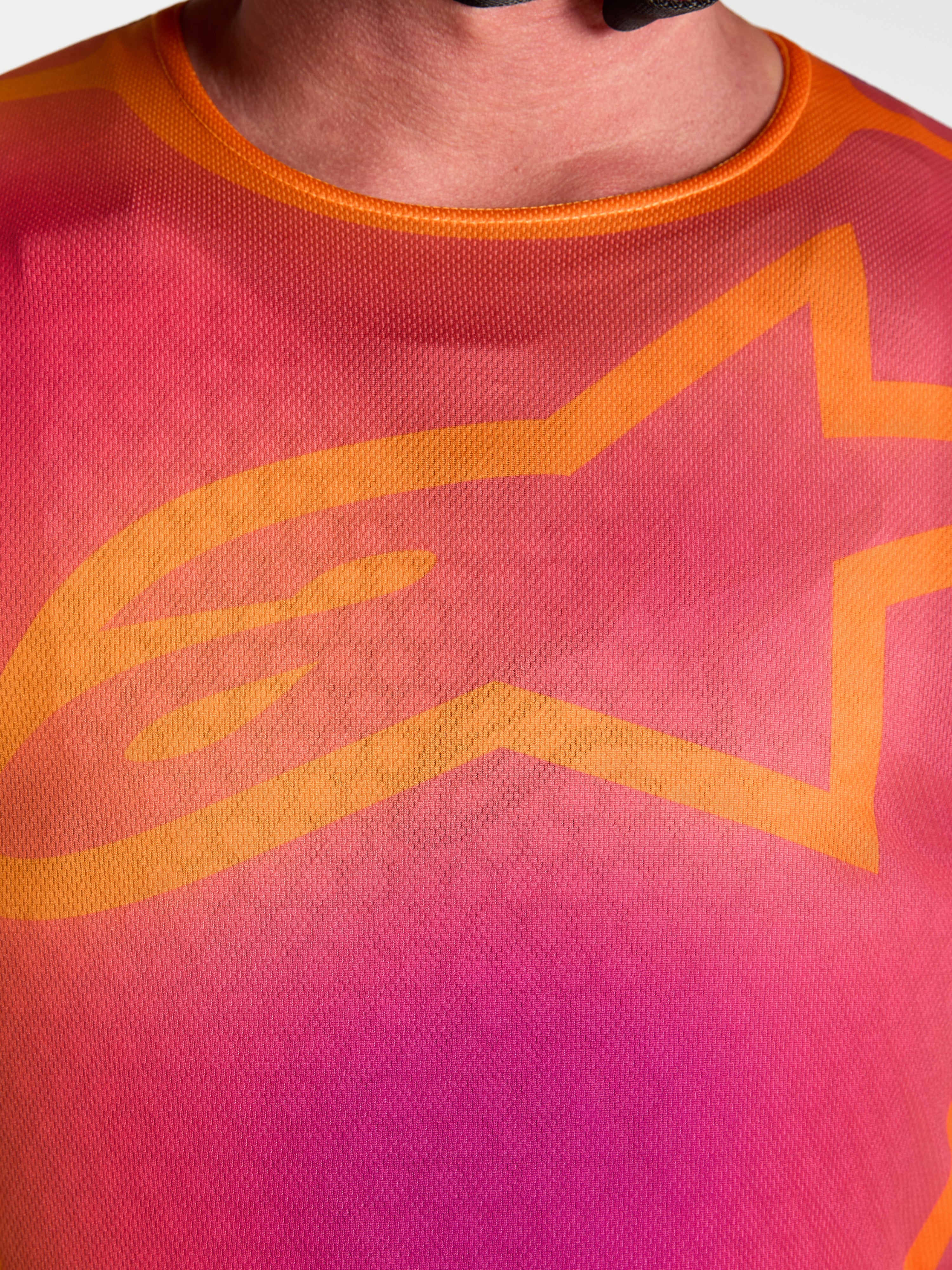 Alpinestars Fluid Kepler tröja, närbild på bröstet i lila och orange med ikonisk orange A-star-logotyp, fuktavledande polytyg för motocross och terrängkörning.