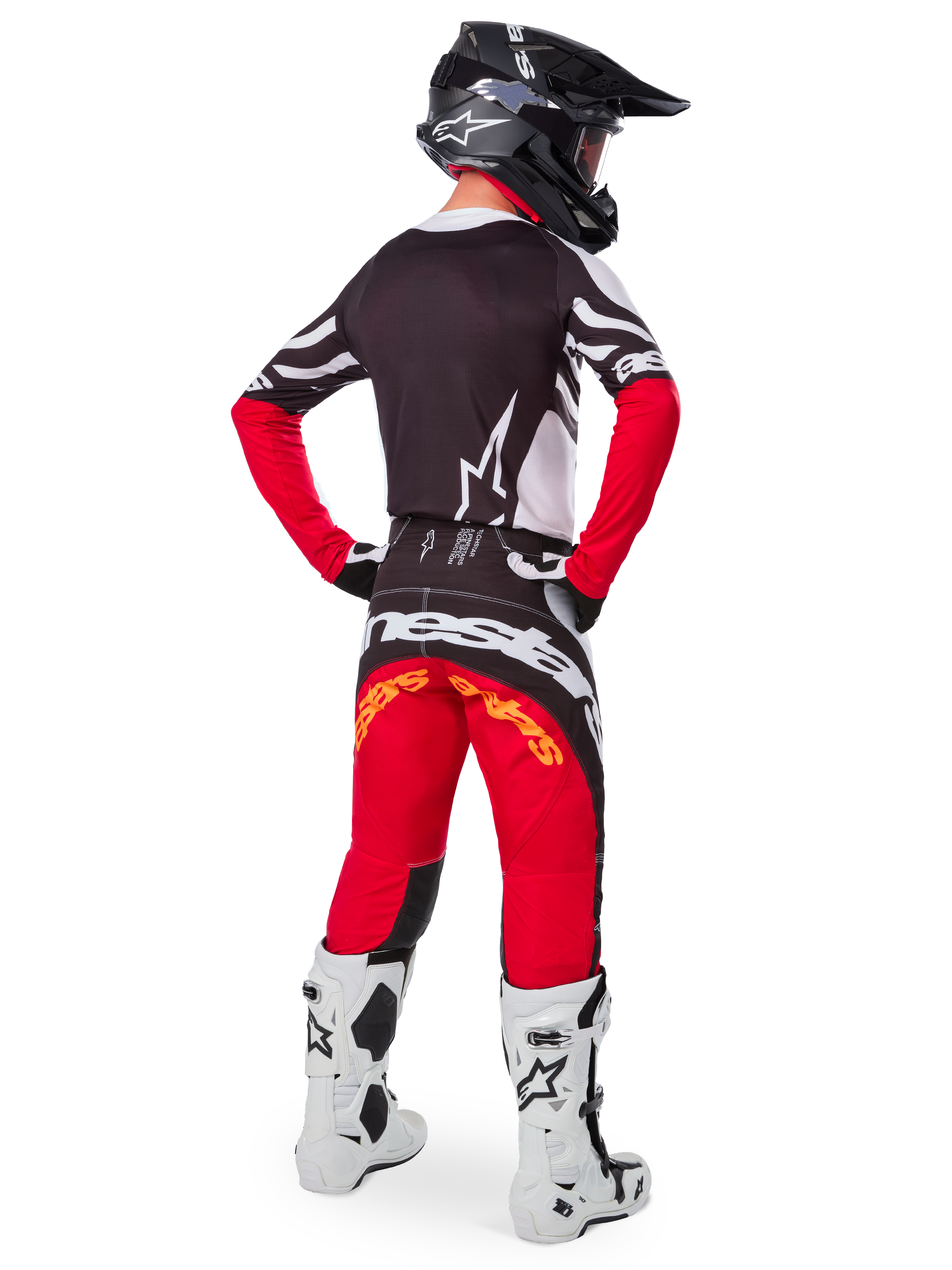 Motocross rider from the rear wearing the Alpinestars Limited Edition Techstar Deep Jersey in Black White High Red, featuring a black back with white star logo and red sleeves, paired with matching red and black pants, white and black boots, and a black helmet for a complete off-road racing outfit.