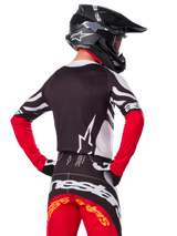 Motocrossförare sedd bakifrån bärande Alpinestars Limited Edition Techstar Deep Jersey, svart, vit och High Red, med matchande racingbyxor och en svart hjälm, atletisk passform för terrängprestanda