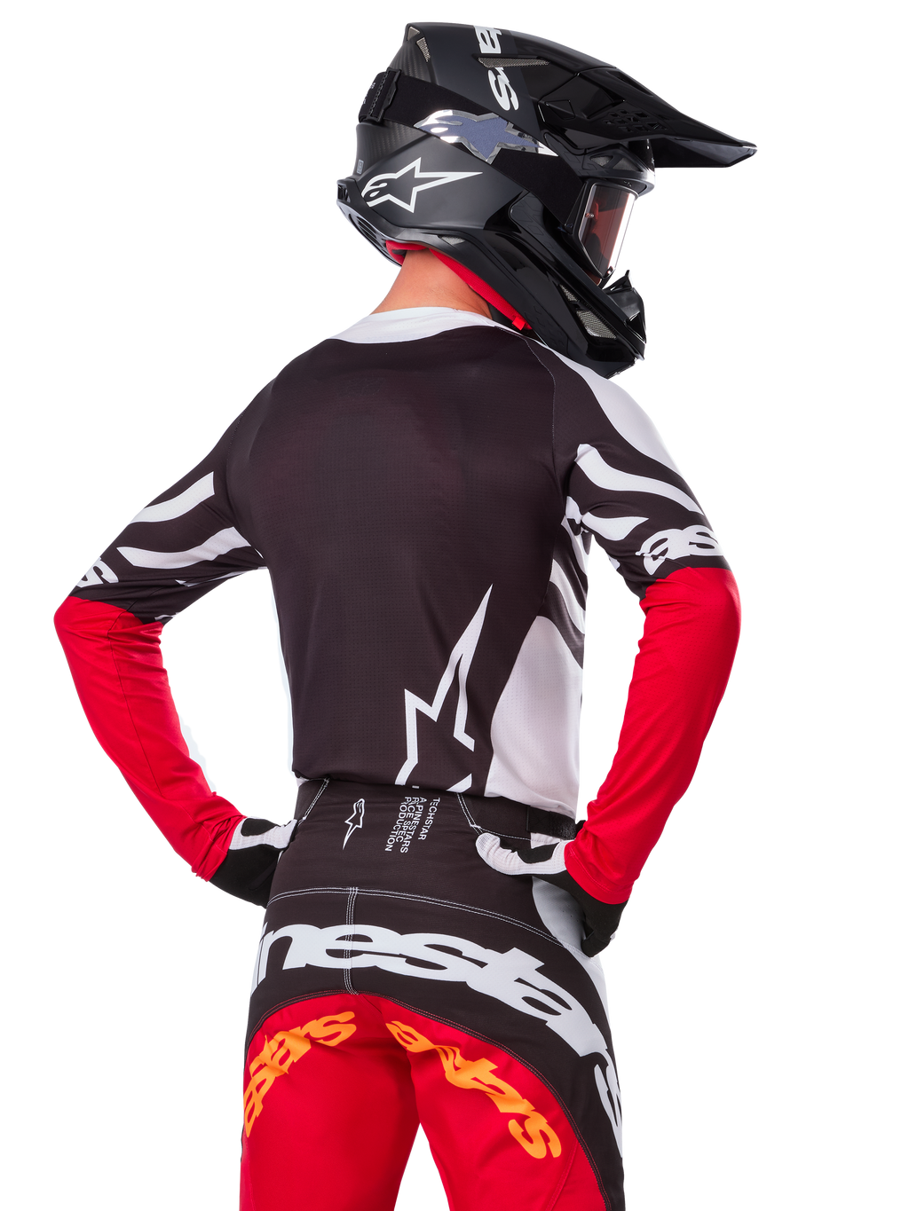 Motocrossförare i komplett racingutrustning, Alpinestars Limited Edition Techstar Deep-tröja i svart, vitt och rött, ryggvy, matchande Techstar Deep-byxor, svart hjälm med goggles, svarta och vita handskar, professionell outfit för terrängkörning