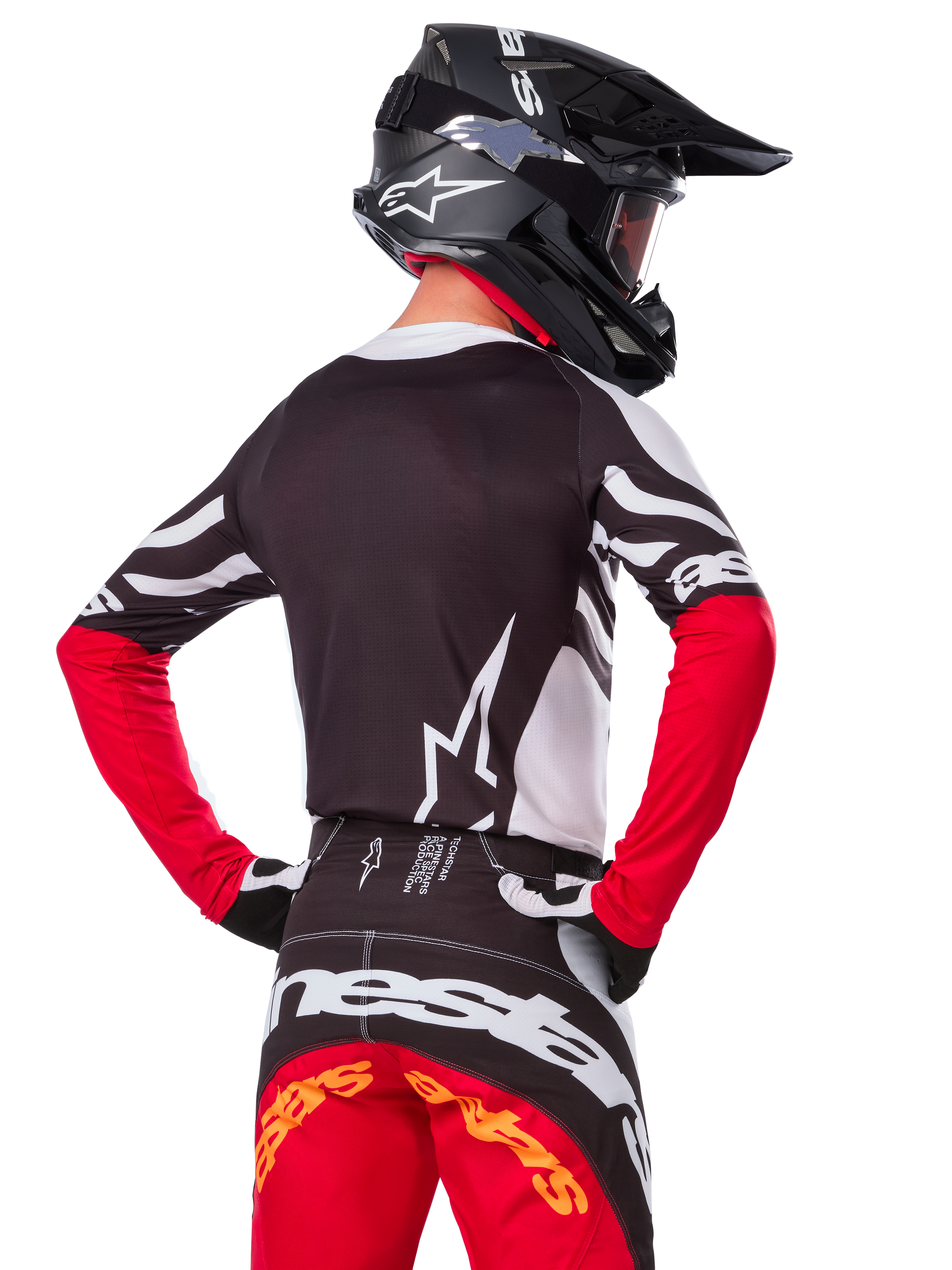 Motocrossförare i komplett racingutrustning, Alpinestars Limited Edition Techstar Deep-tröja i svart, vitt och rött, ryggvy, matchande Techstar Deep-byxor, svart hjälm med goggles, svarta och vita handskar, professionell outfit för terrängkörning