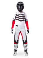 Motocross rider wearing the Alpinestars Limited Edition Techstar Deep Gear Set, white jersey with black wave graphics and red sleeves, matching white and black pants with red inner thigh accents, black helmet with dark goggles, and white boots, full professional off-road racing outfit