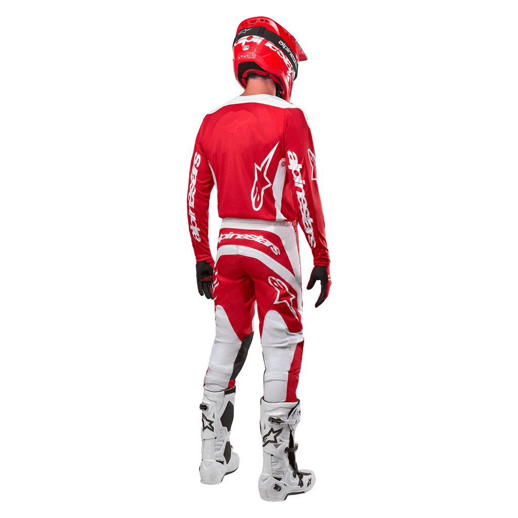Vy bakifrån på en motocrossförare iklädd Alpinestars 2024 Fluid Lurv-tröja i Mars Red White, kombinerad med matchande röda och vita byxor, vita offroad-stövlar och en röd hjälm, som visar tröjans ryggdesign och Alpinestars logotyper.