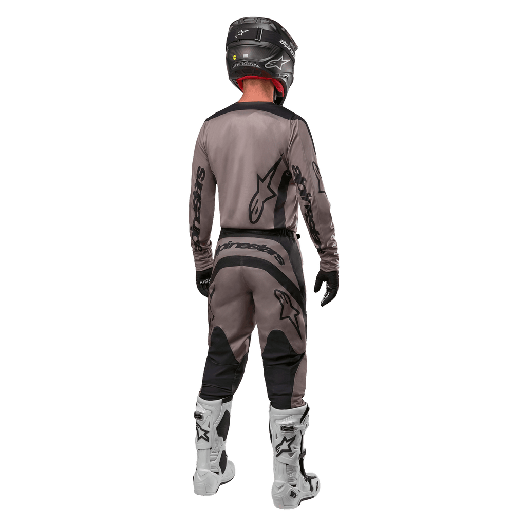 Alpinestars 2024 Fluid Lurv tröja, motocrosströja, Mud Black, bakifrån av en motocrossförare som bär matchande racingutrustning, svart hjälm och vita stövlar, med framträdande svarta Alpinestars-logotyper och en atletisk passform för terrängkörning.
