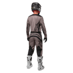 Alpinestars 2024 Fluid Lurv tröja, motocrosströja, Mud Black, bakifrån av en motocrossförare som bär matchande racingutrustning, svart hjälm och vita stövlar, med framträdande svarta Alpinestars-logotyper och en atletisk passform för terrängkörning.