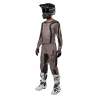 Motocrossförare i komplett racingutrustning med Alpinestars 2024 Fluid Lurv-tröja i Mud Black, matchande byxor, svart hjälm med goggles, vita och svarta stövlar och svarta handskar, koordinerad outfit för terrängkörning