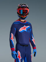 Motocross rider wearing 2026 Supertech Vista Jersey in Dark Navy, Hot Coral, and Cobalt, matching pants and gloves, multi-colored helmet with red goggles, professional gear set for off-road racing