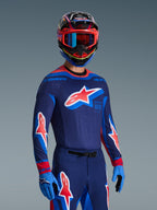 Alpinestars 2026 Supertech Vista-utrustningsset, motocrossförare i mörkblå tröja med ljusblå och röda detaljer och en stor stjärnlogotyp på bröstet, matchande byxor och handskar, flerfärgad hjälm med blå och röda goggles, racingkläder på proffsnivå
