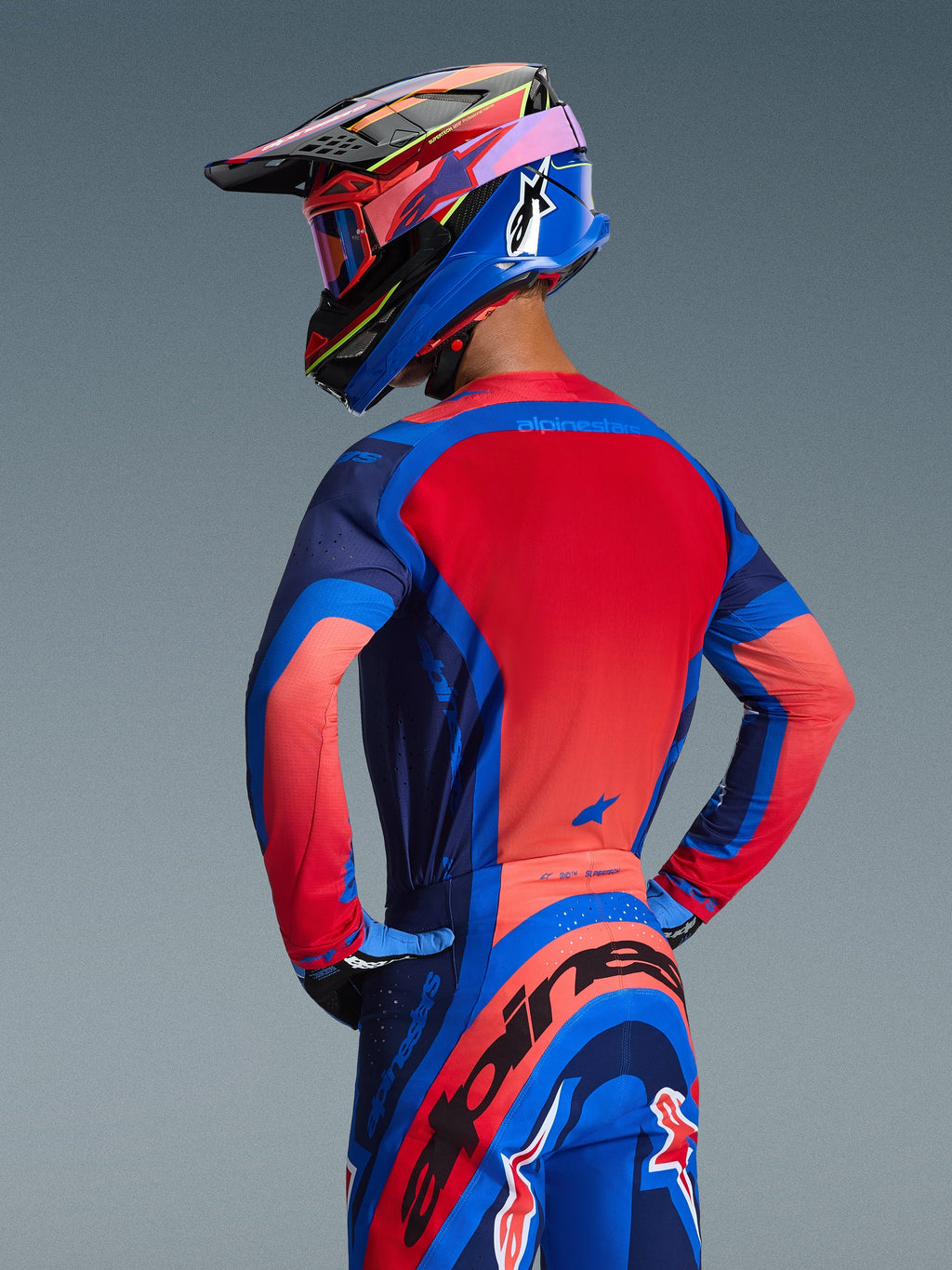 Alpinestars 2026 Supertech Vista-tröja, bakifrån på en motocrossförare, färgerna Dark Navy, Hot Coral och Cobalt, livfull röd ryggpanel och sömlös konstruktion, matchande byxor och hjälm för en komplett racinglook.
