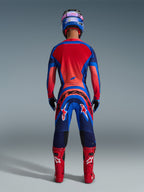 Motocrossförare sedd bakifrån, klädd i Alpinestars 2026 Supertech Vista-tröja i Dark Navy, Hot Coral och Cobalt, matchande set med byxor, röda racingstövlar och blå hjälm, professionell racingutrustning för terrängkörning.