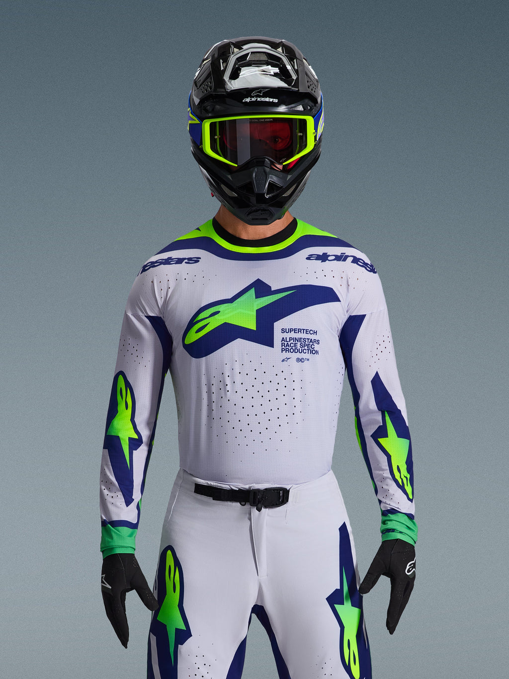 Alpinestars 2026 Supertech Vista tröja, motocrosströja, ljusgrå, gul fluo och blå, bärs av en förare med matchande byxor och svart hjälm, med en stor bröstlogotyp och laserskurna perforeringar för ventilation, atletisk passform på proffsnivå