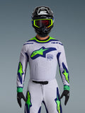 Alpinestars 2026 Supertech Vista tröja, motocrosströja, ljusgrå, gul fluo och blå, bärs av en förare med matchande byxor och svart hjälm, med en stor bröstlogotyp och laserskurna perforeringar för ventilation, atletisk passform på proffsnivå