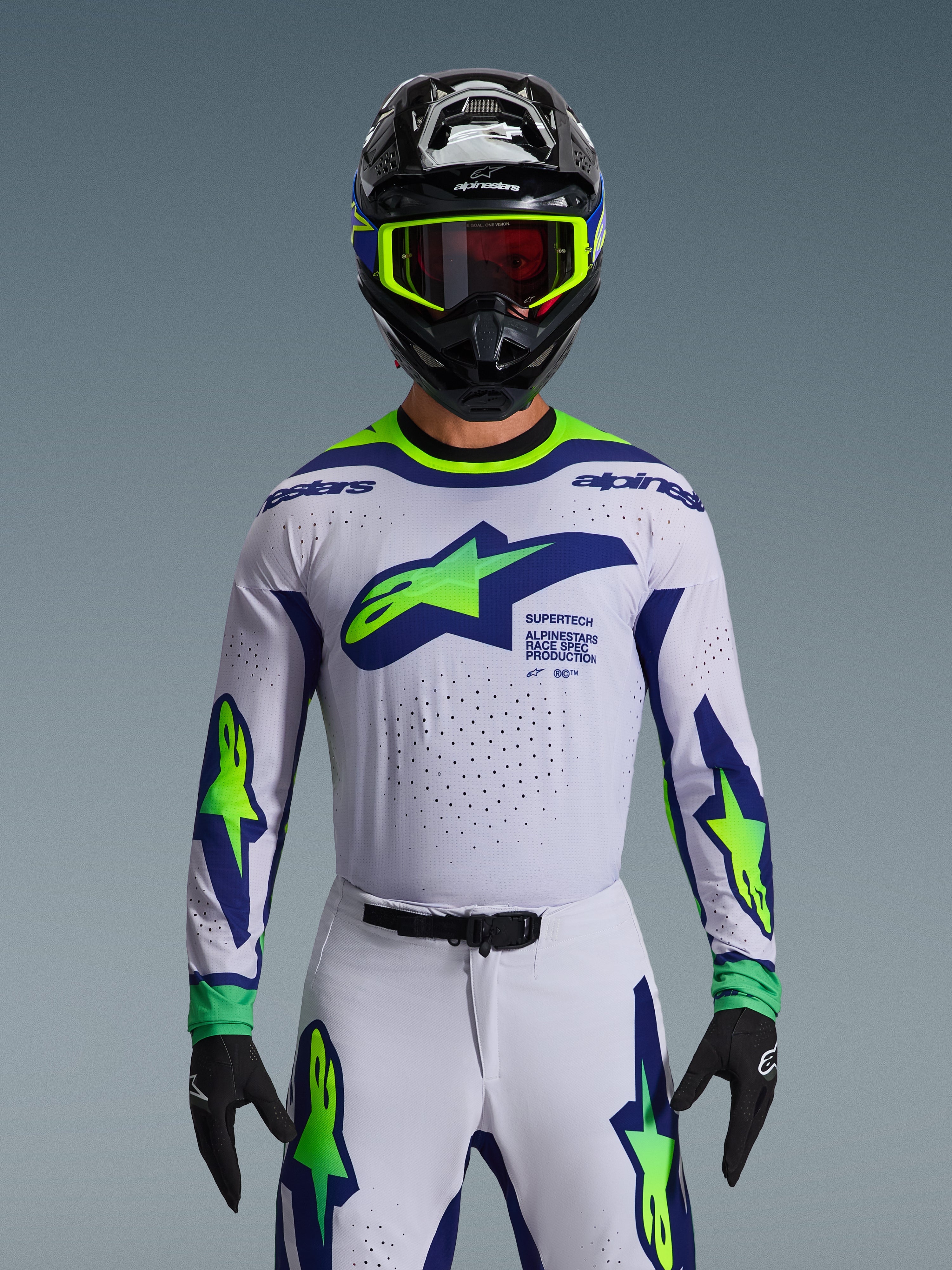 Alpinestars 2026 Supertech Vista tröja, motocrosströja, ljusgrå, gul fluo och blå, bärs av en förare med matchande byxor och svart hjälm, med en stor bröstlogotyp och laserskurna perforeringar för ventilation, atletisk passform på proffsnivå