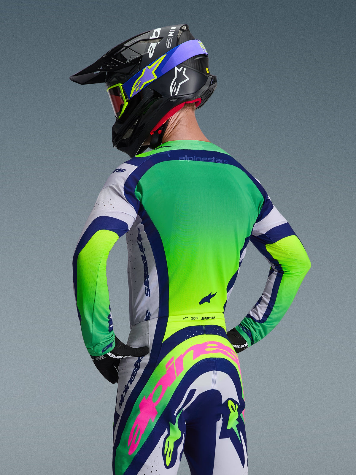 Motocrossförare sedd bakifrån i Alpinestars 2026 Supertech Vista-tröja i Light Gray Yellow Fluo Blue, matchande motocrossbyxor och hjälm, med livfulla neonpaneler och atletisk tävlingspassform för terrängkörning.