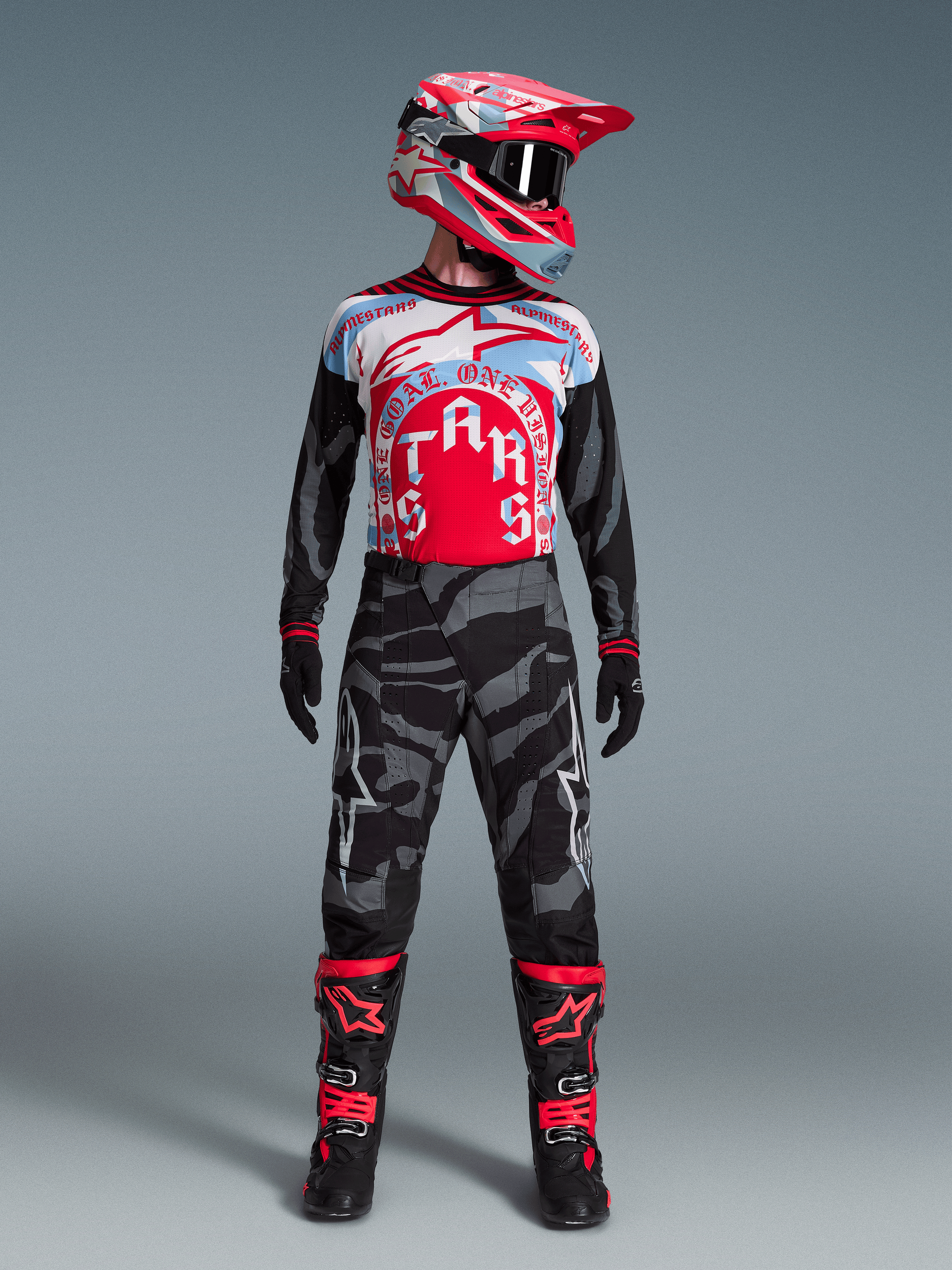Alpinestars Techstar Beast Coast-ställ, röd/blå tröja, grå kamouflagebyxor, matchande hjälm och svarta racingstövlar.
