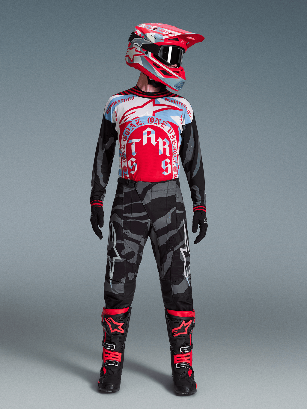 Alpinestars Techstar Beast Coast utrustningsset, förare i röd-blå tröja, kamouflagebyxor, röd hjälm och svarta stövlar.