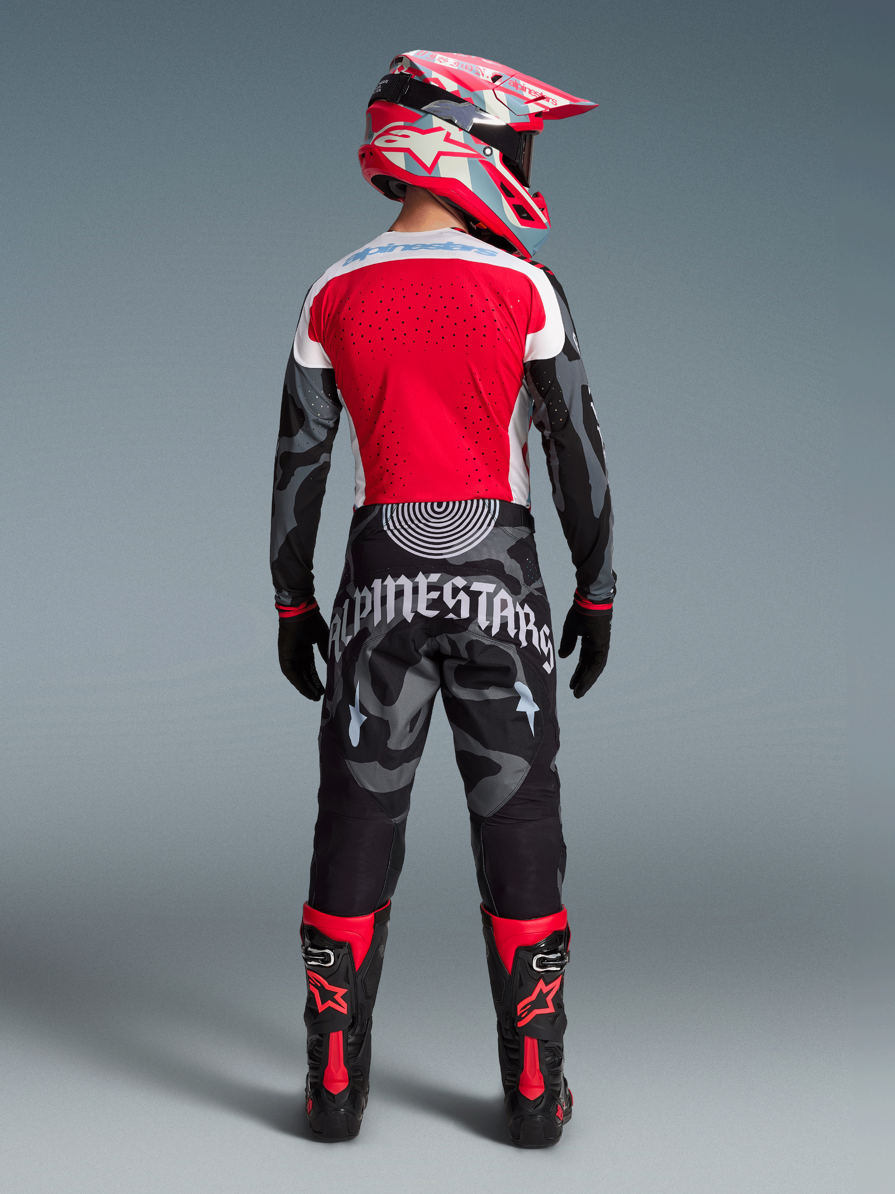 Alpinestars Techstar Beast Coast motocrossbyxor i rött och svart kamouflage, matchande tröja och stövlar sedda bakifrån.