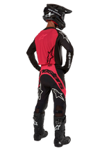 Motocross rider from behind wearing the 2024 Supertech Ward Jersey in Black Red Berry, featuring a vibrant red back panel and black sleeves with white Alpinestars branding. Paired with matching motocross pants, black Tech 10 boots, and a black carbon fiber helmet for a coordinated professional racing gear set.