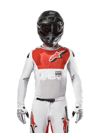 Motocrossförare som bär Alpinestars 2024 Supertech Ward Jersey i White Hot Orange, vit stretchig mesh-tröja med framträdande röd bröstgrafik och logotyp, svart hjälm med mörka goggles, vita handskar, professionell utrustning för terrängkörning