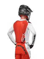 Motocrossförare i 2024 Supertech Ward Jersey i White Hot Orange, sedd bakifrån med orange ryggpanel och vita ärmar med svart Alpinestars-branding, matchad med matchande byxor och en svart hjälm, professionell utrustning för terrängkörning