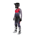 Motocross rider wearing complete racing gear, Alpinestars 2024 Supertech Dade Jersey in Iron Red Berry and grey, matching grey pants with red accents, black helmet with goggles, white and black boots, black gloves, coordinated outfit for off-road racing