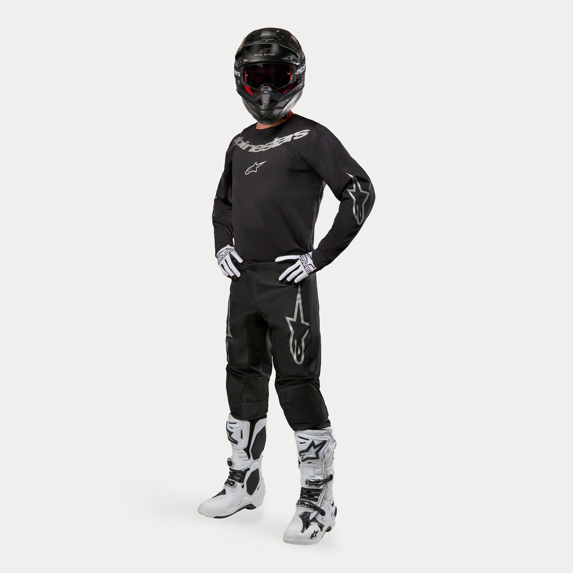 Motocross rider wearing Alpinestars 2024 Fluid Graphite Jersey in Black and Silver, matching black pants with silver star logos, white and black boots, white and black gloves, and a black helmet with red goggles, full off-road racing gear