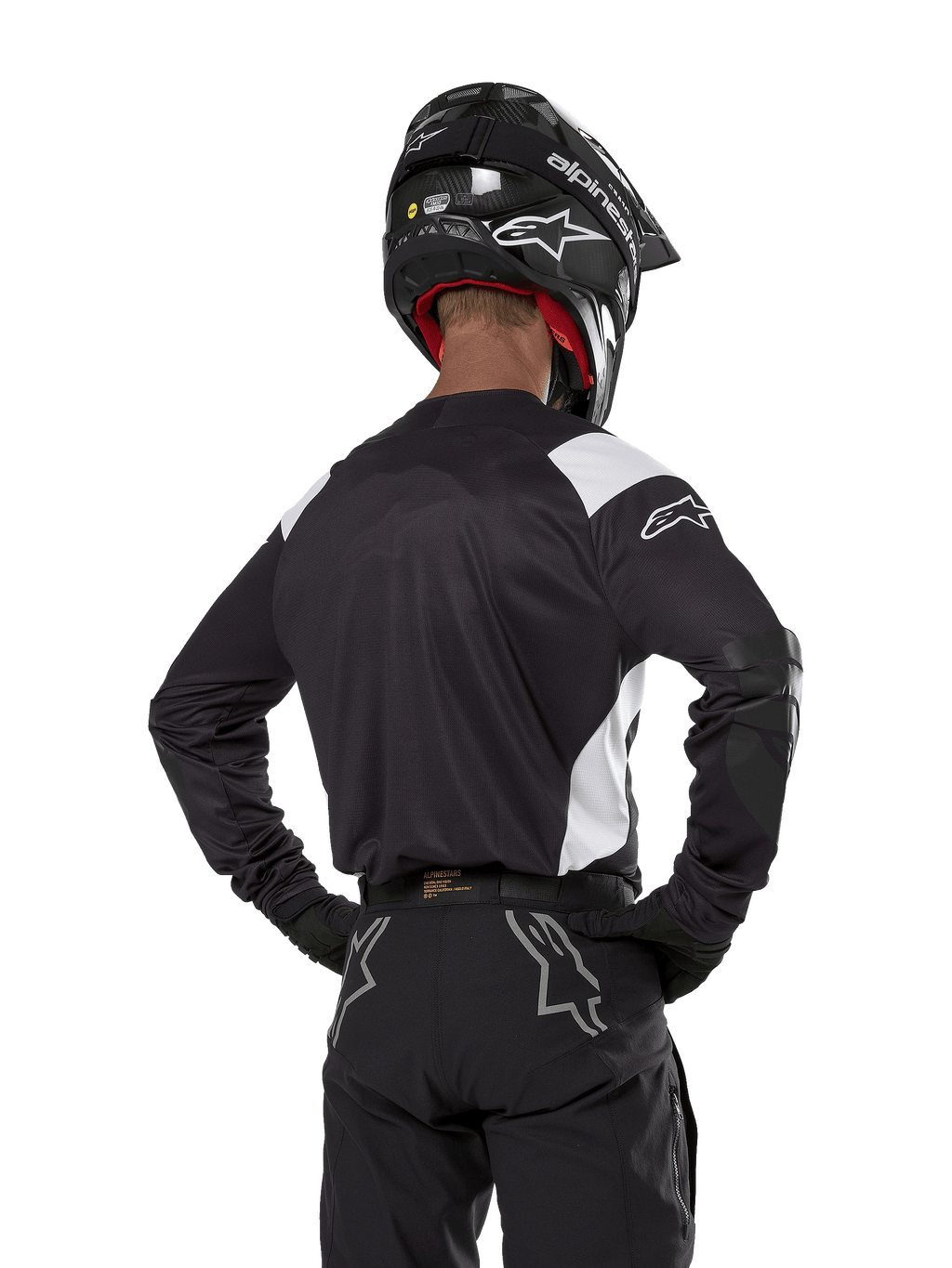 Alpinestars Techdura-tröja, svart med vita axeldetaljer, vy bakifrån på en motocrossförare som bär matchande svarta byxor och hjälm, förstärkta armbågspartier, enduro- och terrängkörningsutrustning