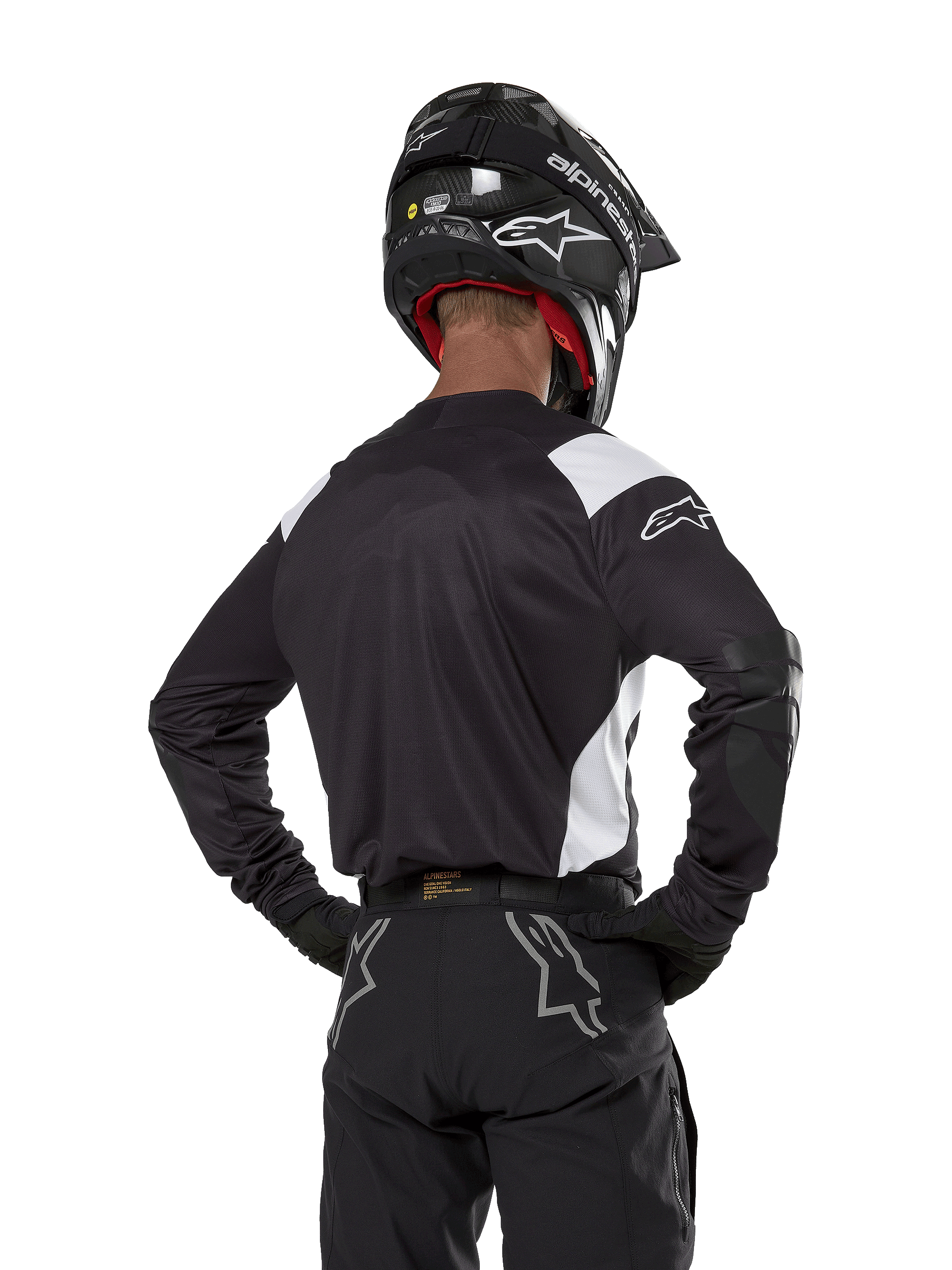 Alpinestars Techdura-tröja, svart med vita axeldetaljer, vy bakifrån på en motocrossförare som bär matchande svarta byxor och hjälm, förstärkta armbågspartier, enduro- och terrängkörningsutrustning
