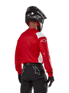 Motocrossförare sedd bakifrån bär Alpinestars Techdura Jersey i klarrött med vita paneler, kombinerat med svarta off-road-byxor, svart hjälm och svarta handskar, koordinerad utrustning för enduro- och motocrosskörning.