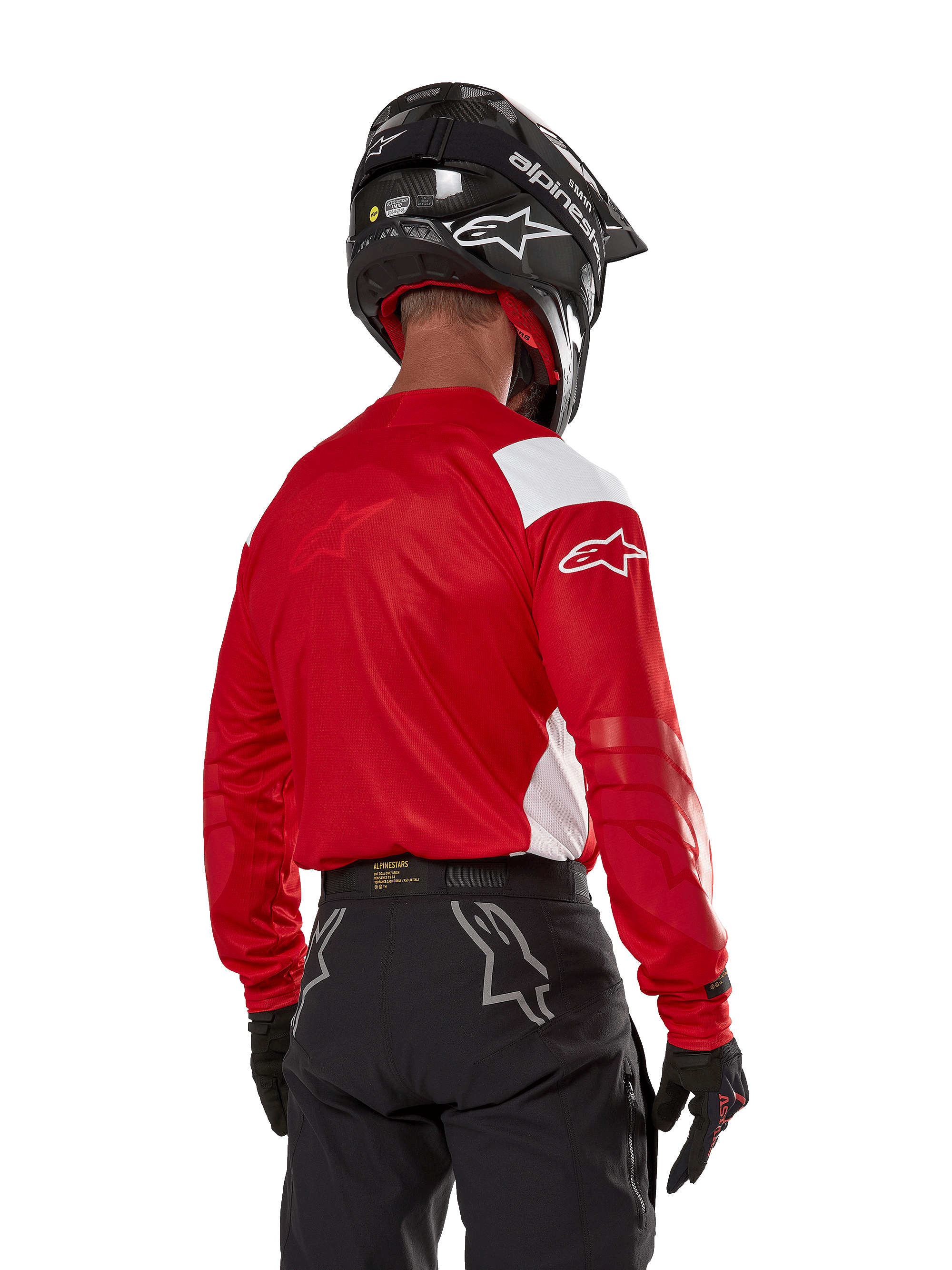 Motocrossförare sedd bakifrån bär Alpinestars Techdura Jersey i klarrött med vita paneler, kombinerat med svarta off-road-byxor, svart hjälm och svarta handskar, koordinerad utrustning för enduro- och motocrosskörning.