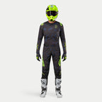 Motocrossförare i komplett racingutrustning, 2024 Techstar Rantera-tröja i Black Navy och Yellow Fluo, matchande byxor med abstrakt tryck, neongul hjälm, vita och svarta stövlar, koordinerad outfit för terrängkörning