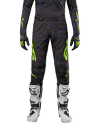 Alpinestars 2024 Techstar Rantera byxor, motocrossbyxor, svart, marinblå och neongul, bärs med matchande långärmad tröja, handskar och vita motocross-stövlar, med framträdande neongula accenter och ett abstrakt mörkt mönster.