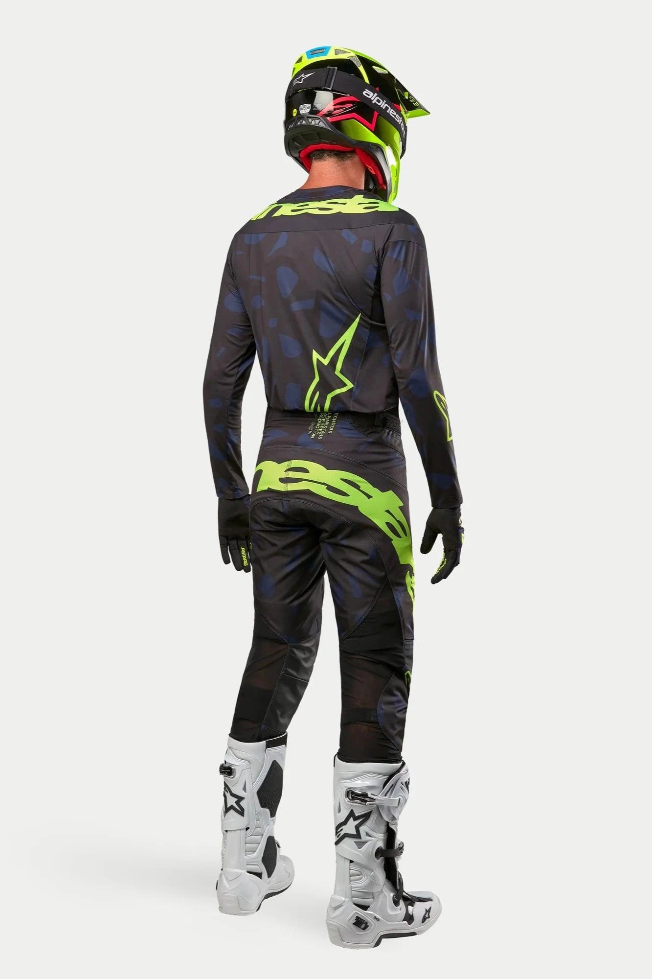 Alpinestars 2024 Techstar Rantera-tröja och byxor, motocrossförare i full utrustning bakifrån, svart, marinblå och neongul, matchande neongul hjälm och vita stövlar, koordinerat racingställ för terrängkörning