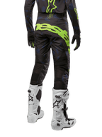 Alpinestars 2024 Techstar Rantera byxor, motocrossbyxor, svarta, marinblå och neongula, vy bakifrån, med framträdande neongul logotyp och ventilationspaneler i mesh, bärs med matchande tröja och vita stövlar, slitstark utrustning för motocross och terrängkörning