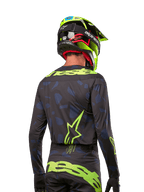 Vy bakifrån av en motocrossförare i Alpinestars 2024 Techstar Rantera Jersey i Black Navy Yellow Fluo, med framträdande neongul branding och logotyper på ryggen, matchad med matchande motocrossbyxor och en neongul hjälm för en komplett offroad-look.