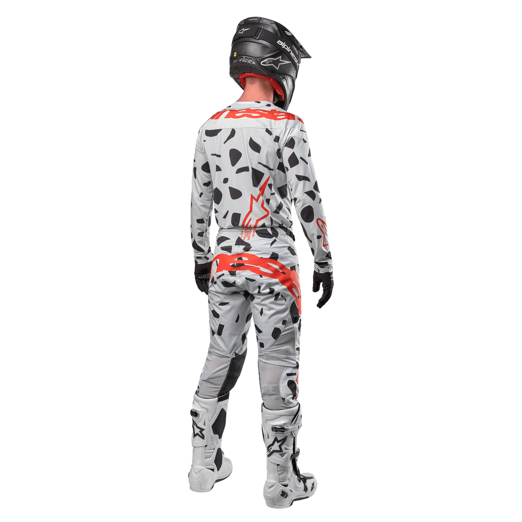Motocrossförare sedd bakifrån bärandes Alpinestars 2024 Techstar Rantera-tröja och matchande byxor, Haze Gray Camo-mönster med framträdande röda Alpinestars-logotyper, svart hjälm, vita och svarta stövlar, svarta handskar, koordinerat set med motocrossutrustning.