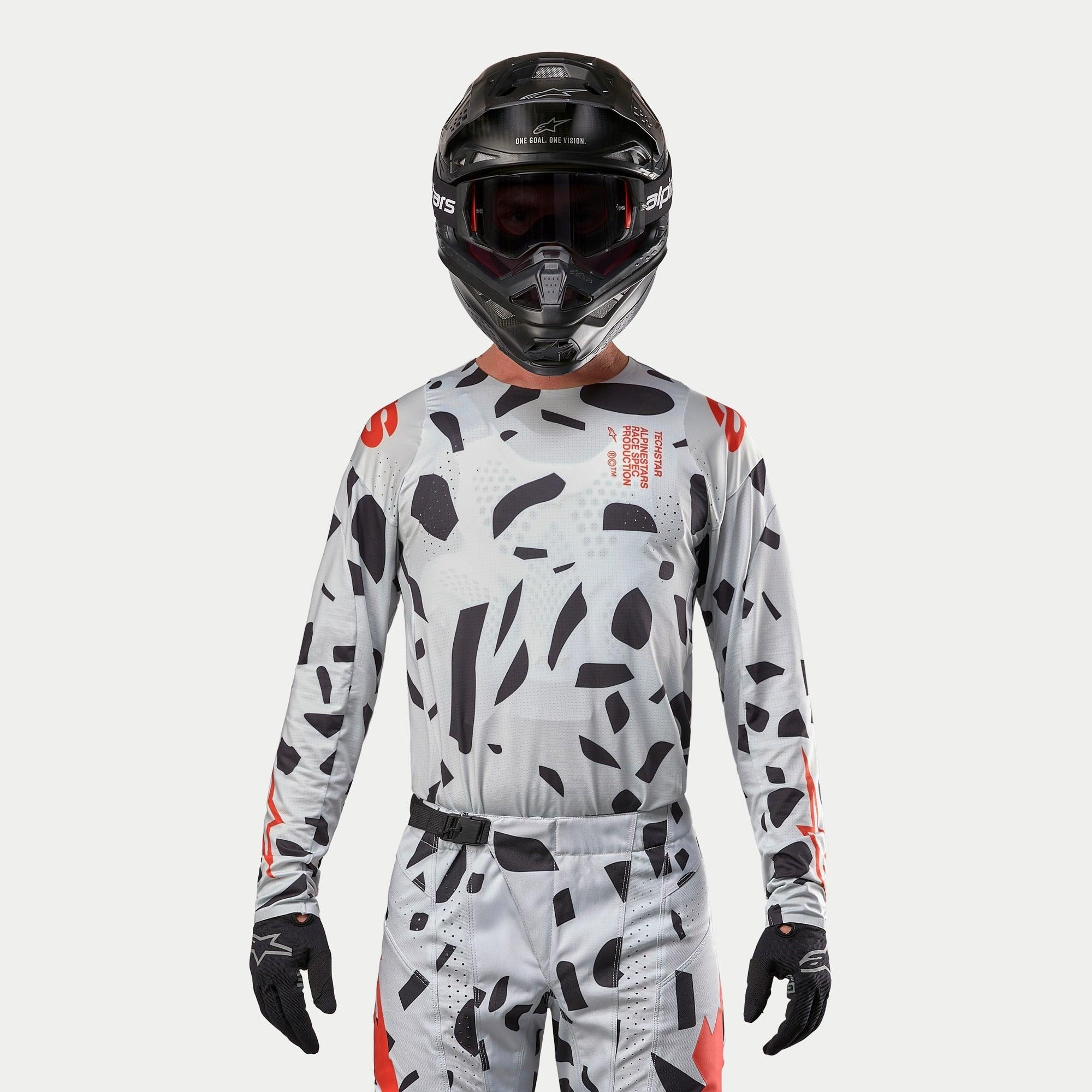 Alpinestars 2024 Techstar Rantera-tröja, motocrosströja, Haze Gray Camo med svarta oregelbundna mönster och röda detaljer, bärs av en förare med matchande byxor, svart hjälm och handskar, utrustning för terrängkörning
