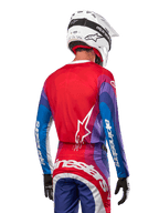 Motocrossförare sedd bakifrån i Alpinestars 2024 Techstar Pneuma Jersey i Blue Mars Red White, med röd rygg och vit stjärnlogotyp, blå och lila ärmar med vit logotyp, matchande byxor och vit hjälm för terrängkörning.