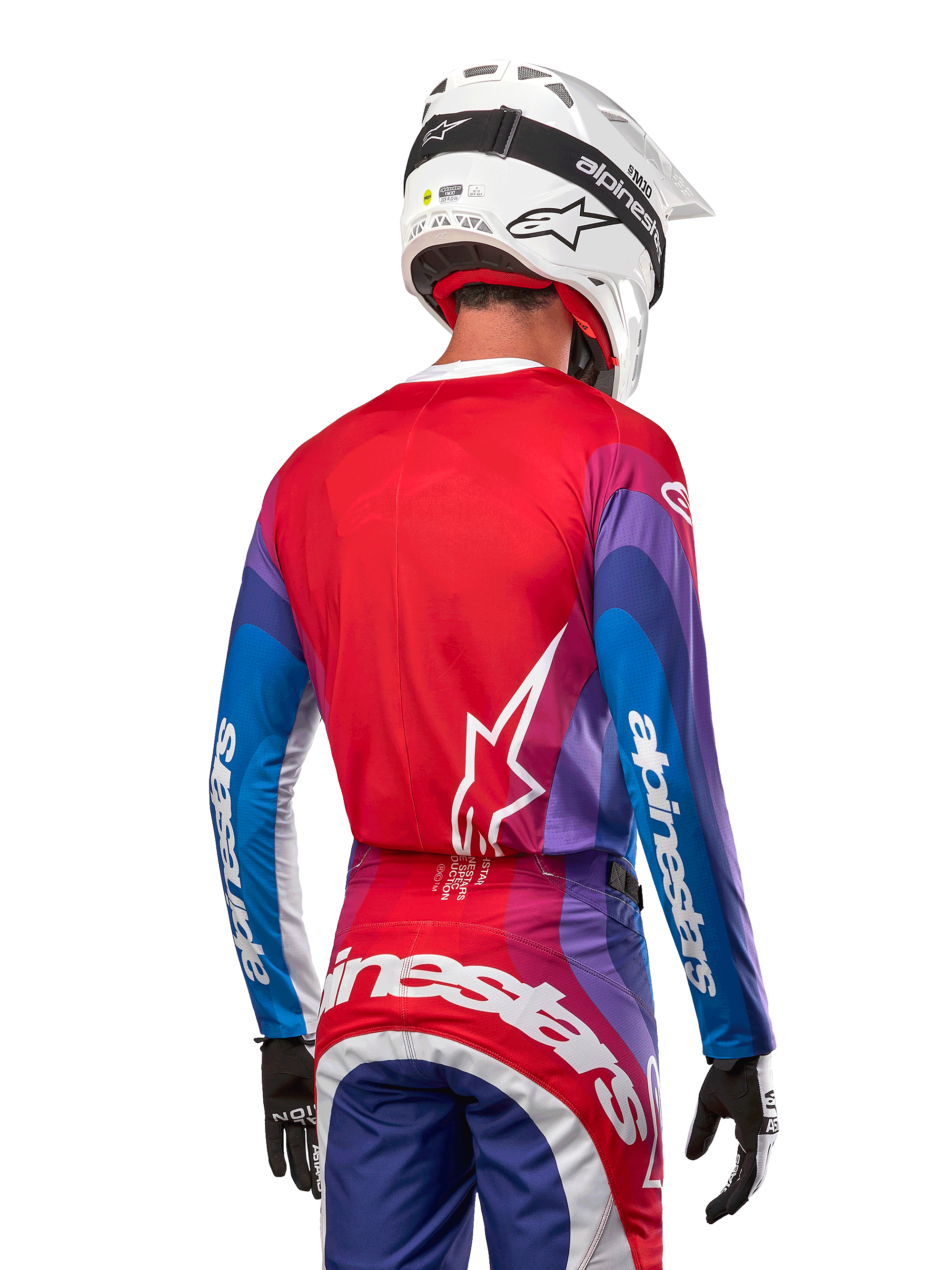 Motocrossförare sedd bakifrån i Alpinestars 2024 Techstar Pneuma Jersey i Blue Mars Red White, med röd rygg och vit stjärnlogotyp, blå och lila ärmar med vit logotyp, matchande byxor och vit hjälm för terrängkörning.