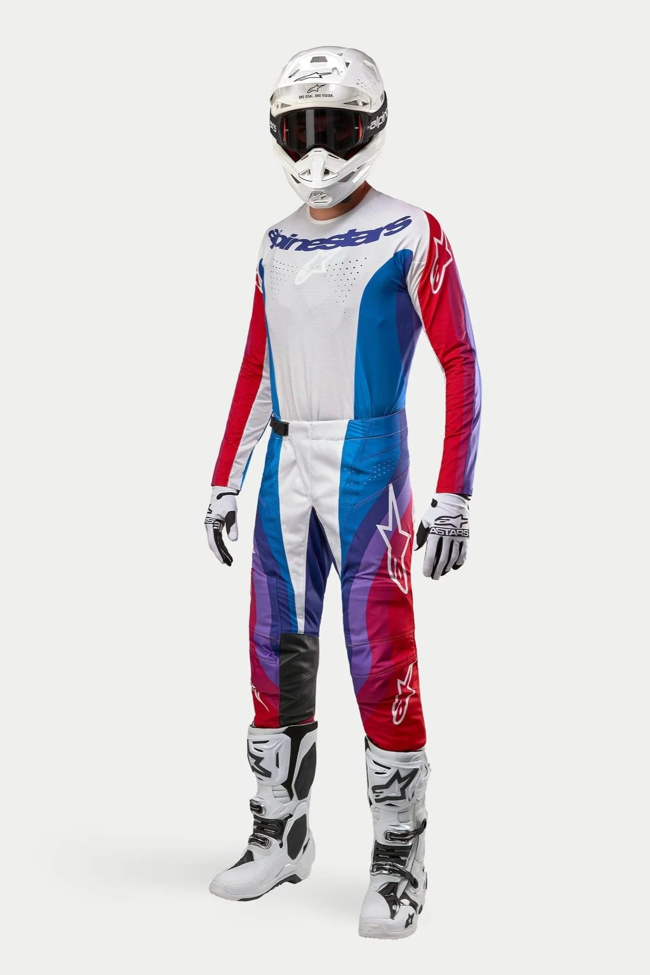 Motocrossförare i komplett Alpinestars-utrustning, 2024 Techstar Pneuma-byxor i Blue Mars Red White, matchande långärmad tröja, vit hjälm med mörka goggles samt vita och svarta stövlar, koordinerad outfit för terrängkörning.
