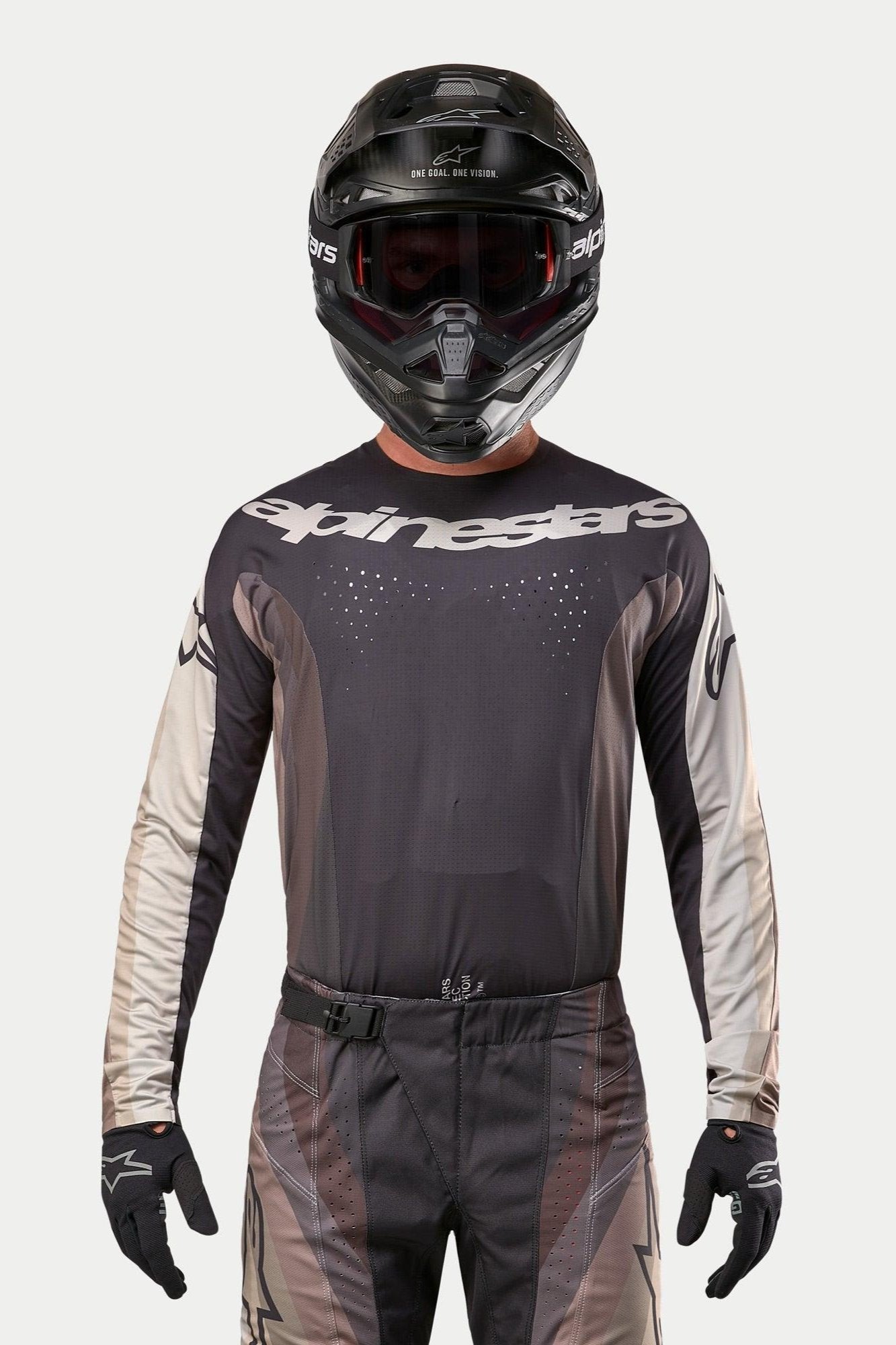 Alpinestars 2024 Techstar Pneuma Jersey, Motocross Jersey, Dark Sand and Iron Dust Gray, worn with matching motocross pants and a black helmet, featuring a prominent Alpinestars logo across the chest and laser-cut ventilation perforations, performance off-road racing gear.