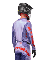 Alpinestars 2024 Techstar Ocuri tröja, motocrosströja, lila och neonorange, vy bakifrån på en förare i matchande utrustning och svart hjälm, med stor orange Alpinestars-text på ärmarna och nedre delen av ryggen