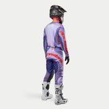 Alpinestars 2024 Techstar Ocuri motocross-set, ryggvy av förare i lila och ljuslila jersey och byxor med detaljer i 'hot orange', röd logotyp på rygg och lår, svart hjälm, vita stövlar och svarta handskar, professionell off-road utrustning.