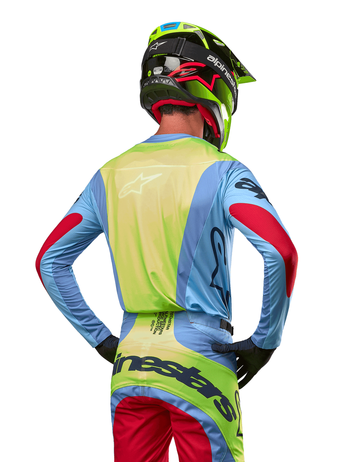 Motocrossförare sedd bakifrån i Alpinestars 2024 Techstar Ocuri-tröja, ljusblå med neongul rygg och röda detaljer på ärmarna, matchande motocrossbyxor och neongul hjälm, koordinerad outfit för terrängkörning