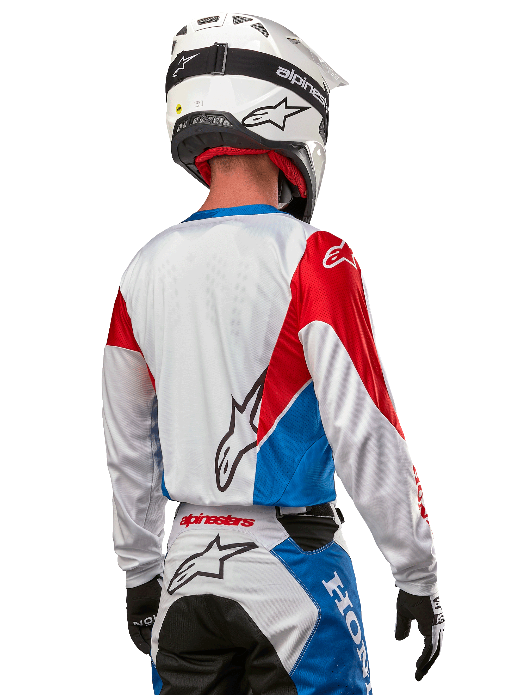 Motocrossförare i Alpinestars Honda Racer Iconic-tröja, sedd bakifrån, vit med klarblå och klarröda paneler, framträdande Alpinestars-logotyp på ryggen, kombinerat med vit motocrosshjälm och matchande racingbyxor.